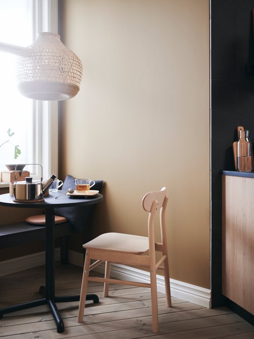 Dining area with a round table made of steel and particleboard, a grey kettle placed on top and a beige pendant lamp above.