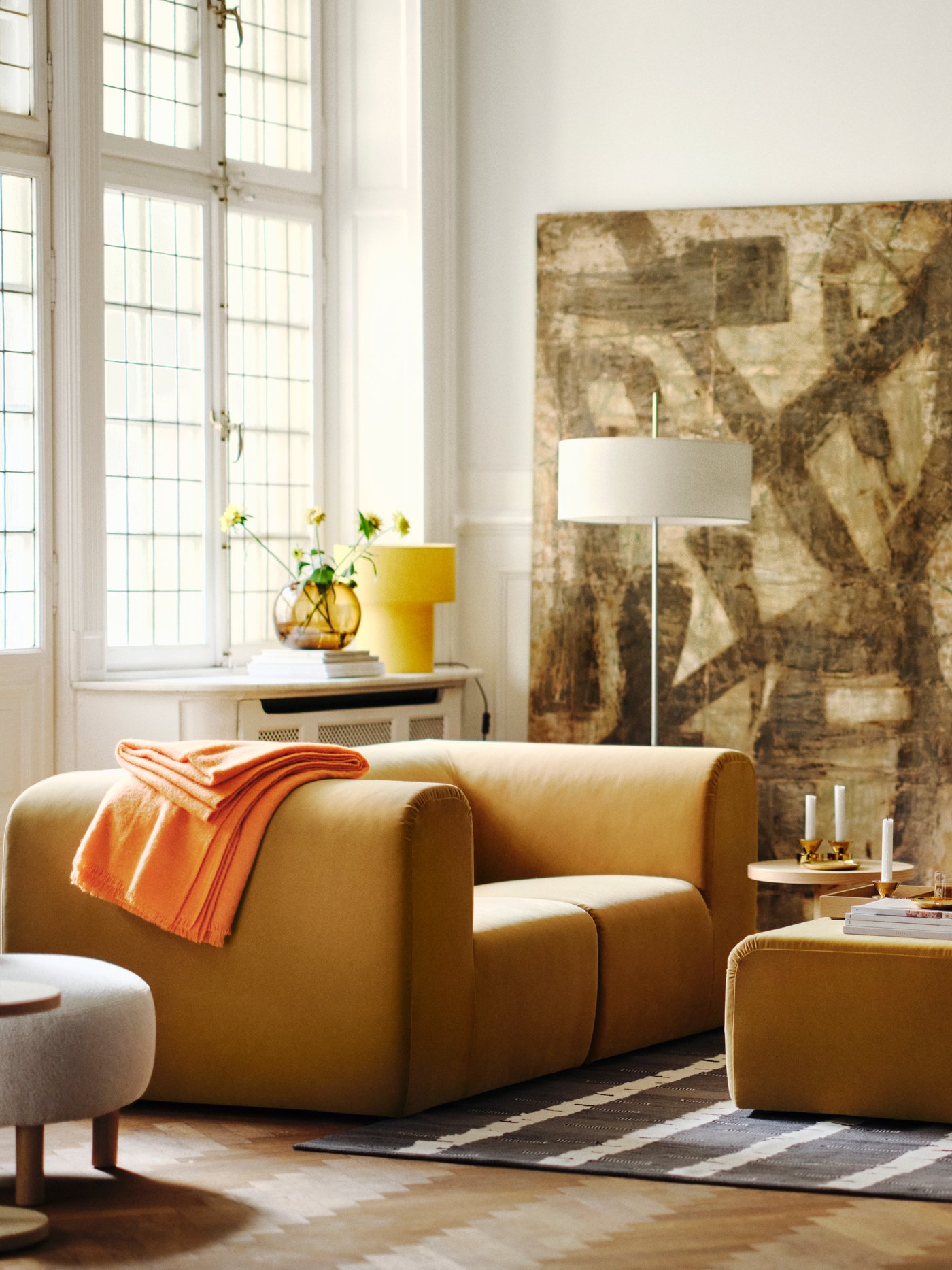 Un salon lumineux avec deux canapés 2 places STOCKHOLM 2025 beiges placés face à face, avec un pouf sur un tapis entre les deux.