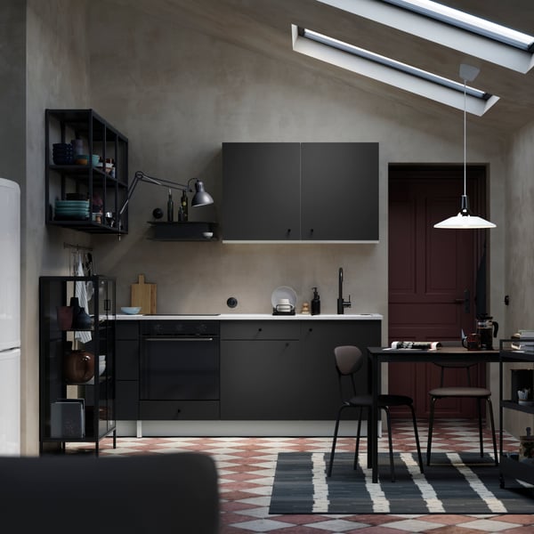 Un espace élégant et monochrome avec une cuisine KNOXHULT en gris foncé, un plafond incliné et un coin repas.