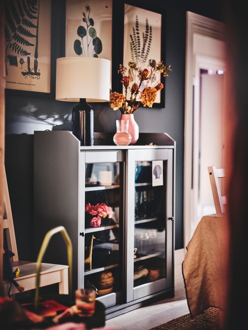 Hallway area featuring a grey glass door cabinet containing items, with a table lamp and a vase on the top shelf.