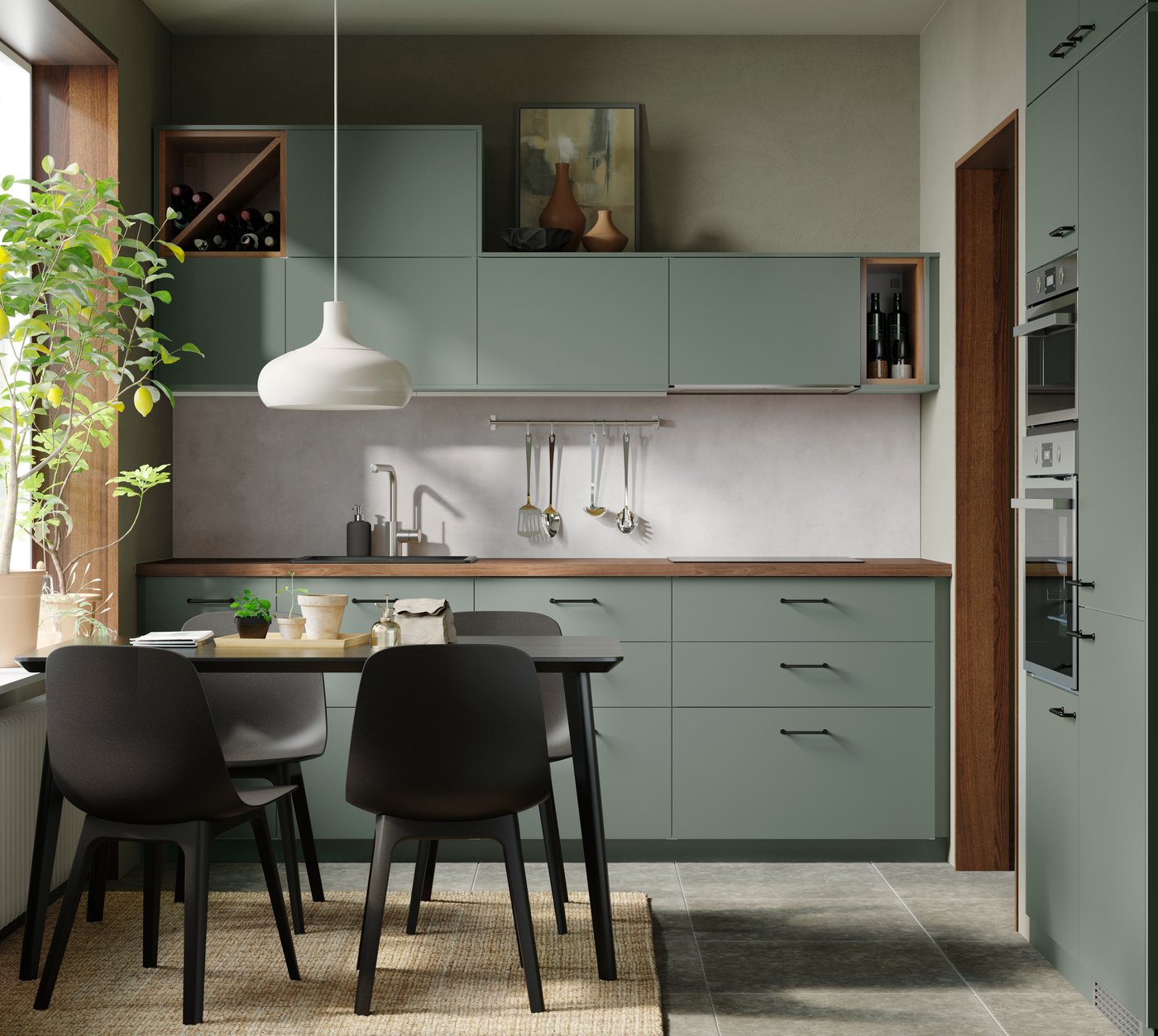 緑のキャビネットと木製天板のキッチン。ダイニングテーブルと黒い椅子、窓際には植物が飾られている。