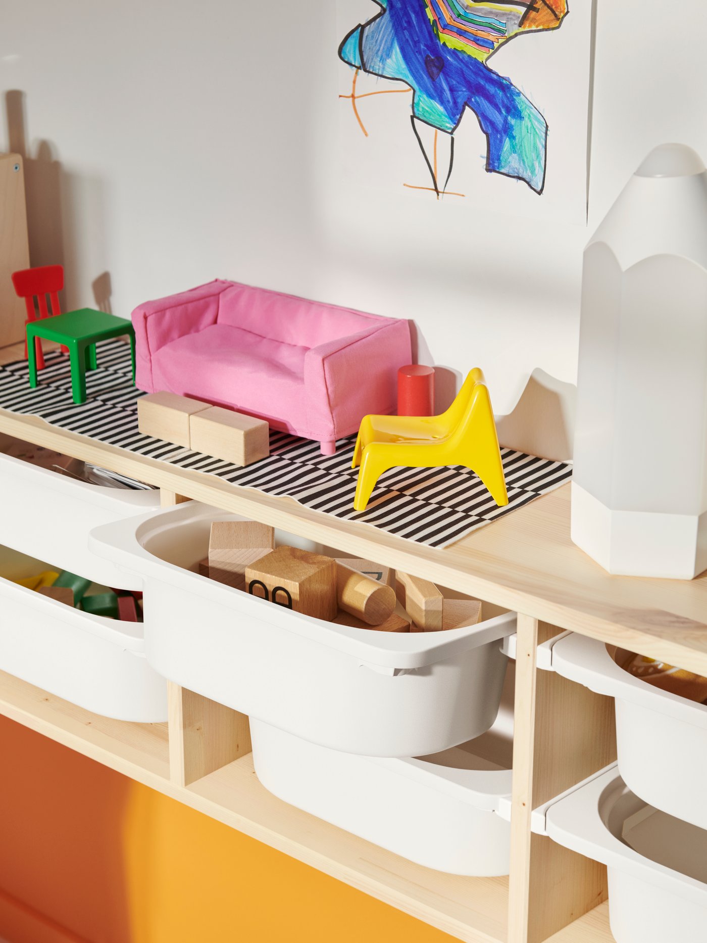 Various colourful toys on top a light white stained pine TROFAST wall storage filled with white storage boxes.