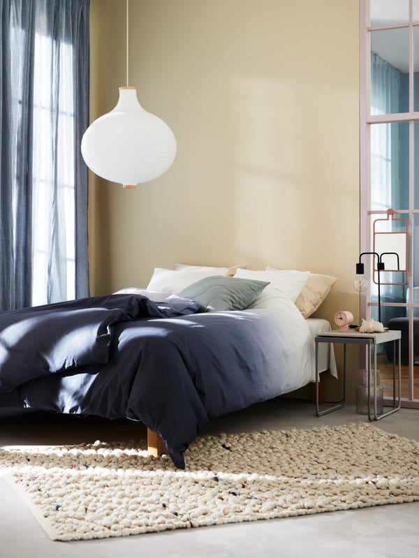 A double bed made with STRANDTRIFT duvet cover featuring a gradient of blues and white, placed in a light-yellow bedroom.