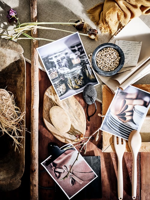 Rustikale Holztischplatte mit getrockneten Blumen, Fotos, Stroh, einer Schüssel, einem Holzlöffel, einer Gabel und einem Schneidebrett.