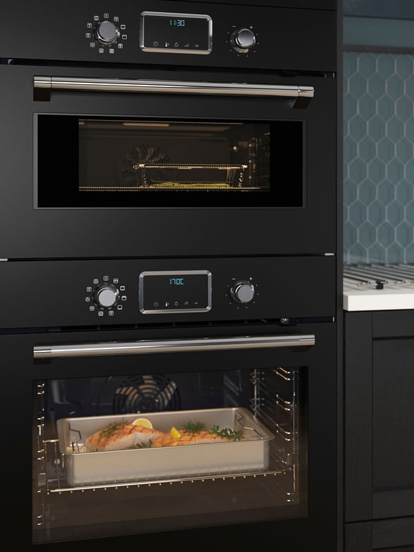 A FORNEBY forced-air oven in black and roasting tin of food inside, and a FORNEBY combi microwave oven in black above.