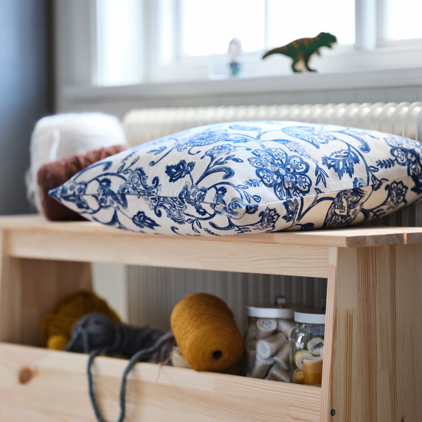 مقعد مع تخزين PERJOHAN مع مكان للتخزين أسفل نافذة وألعاب في حجيرات ووسادة كبيرة في الأعلى عليها رسومات.