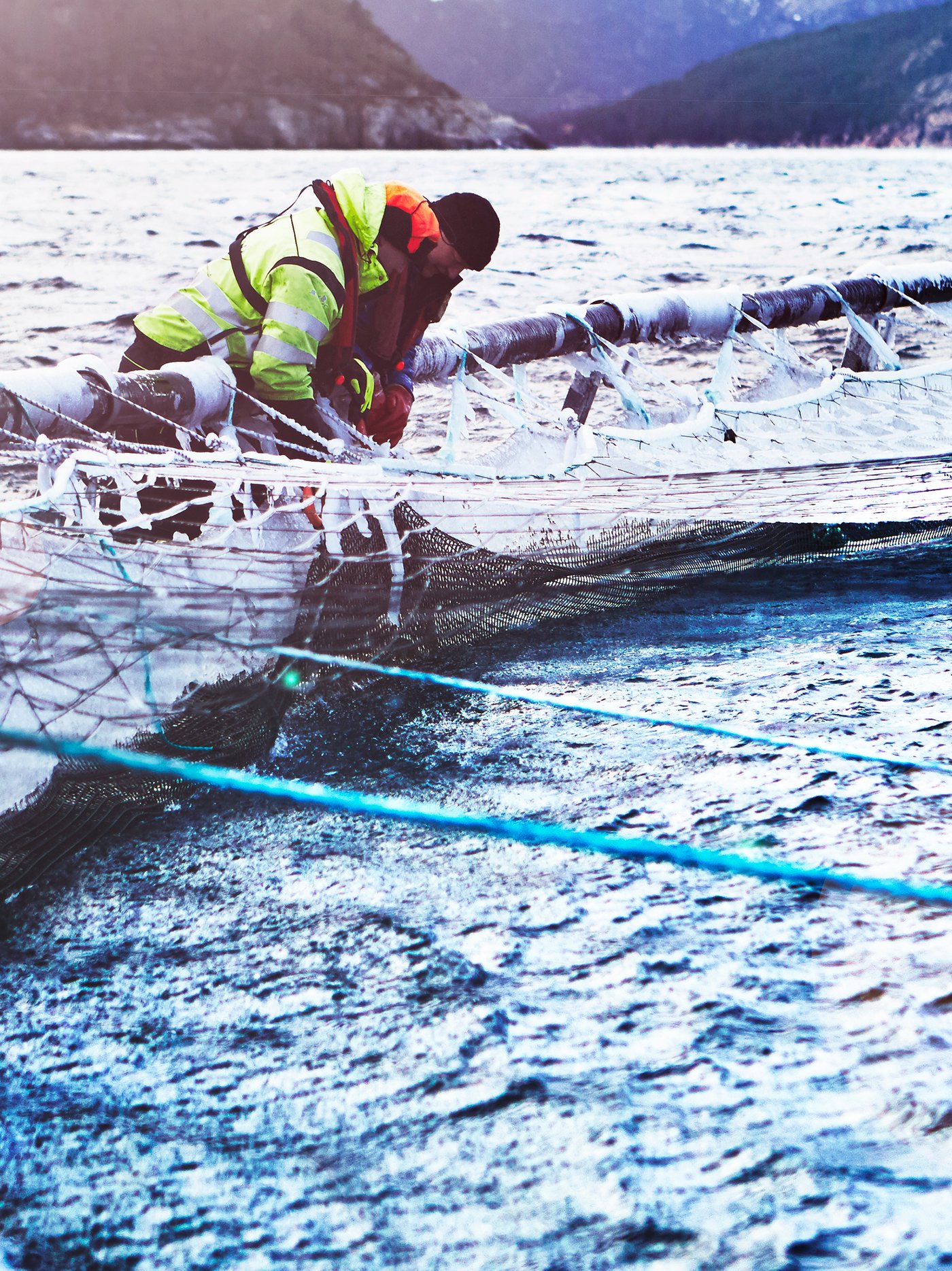 Two salmon farm workers dressed in heavy outdoor clothing tending a fish enclosure on a Norwegian salmon farm.