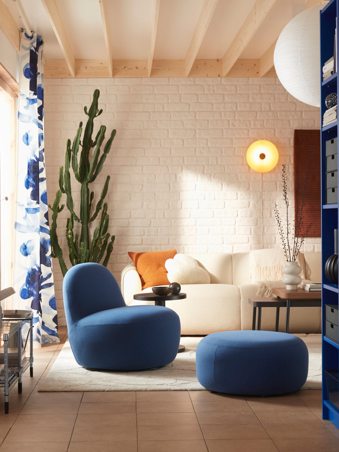 Un soggiorno con una poltrona girevole LILLESÄTER in tessuto morbido blu scuro Gunnared accanto a un divano bianco sporco e piante verdi.