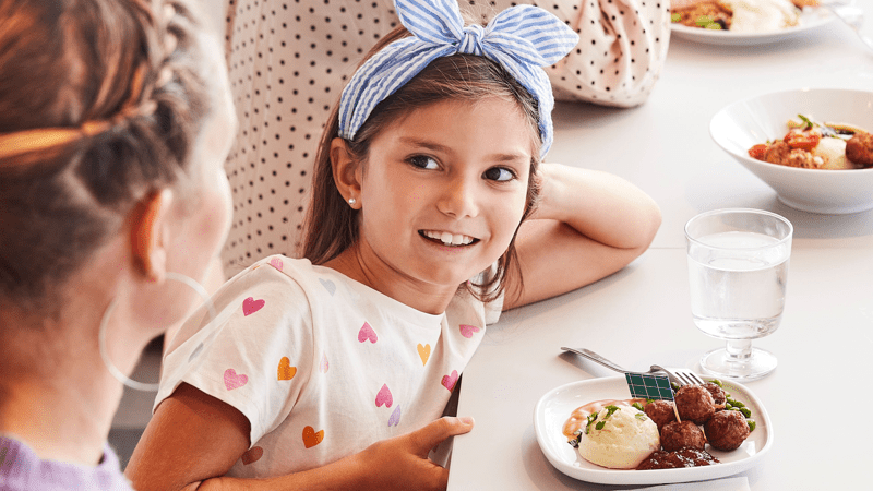 Twee kinderen zitten aan tafel met een bordje vleesballetjes, puree en saus.