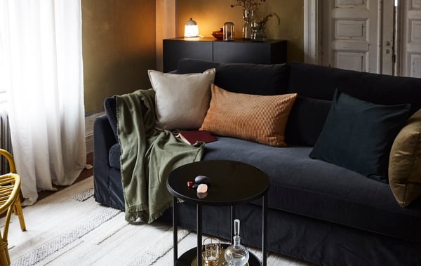 Ein Wohnzimmer mit einem dunklen Sofa und Kissen und Decken in herbstlichen Farben. 