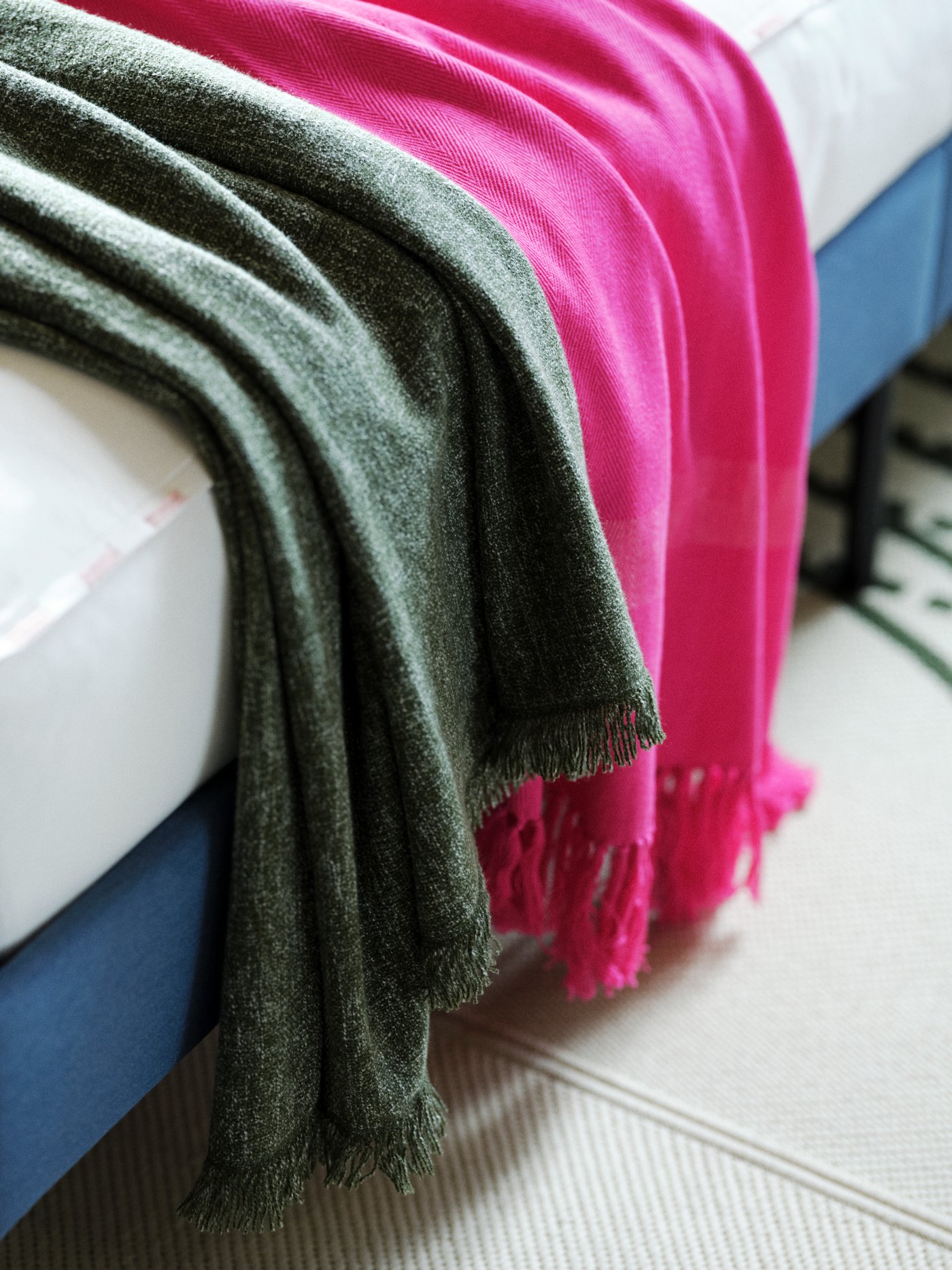 A pink HILLEGÄRD throw and a dark green INGRUN throw on a blue BLÅKULLEN upholstered bed.