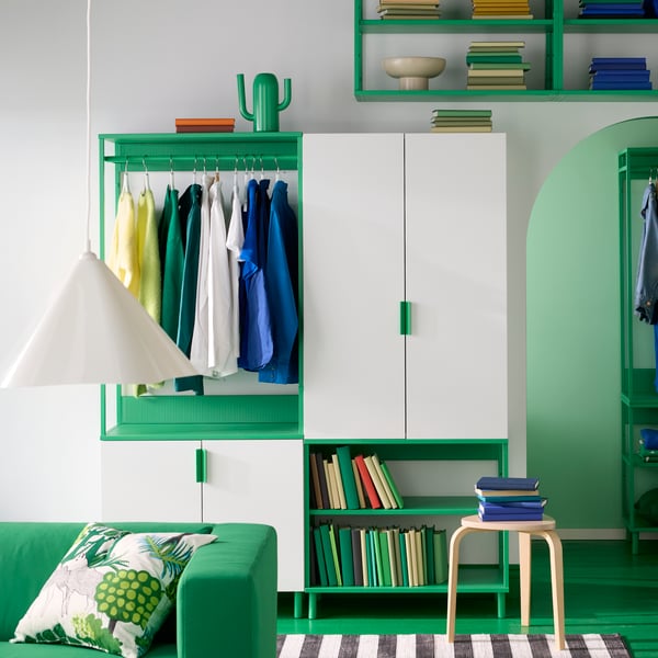 A white and green PLATSA wardrobe with 4 doors against a white wall holds clothes and books. A birch stool sits before it.