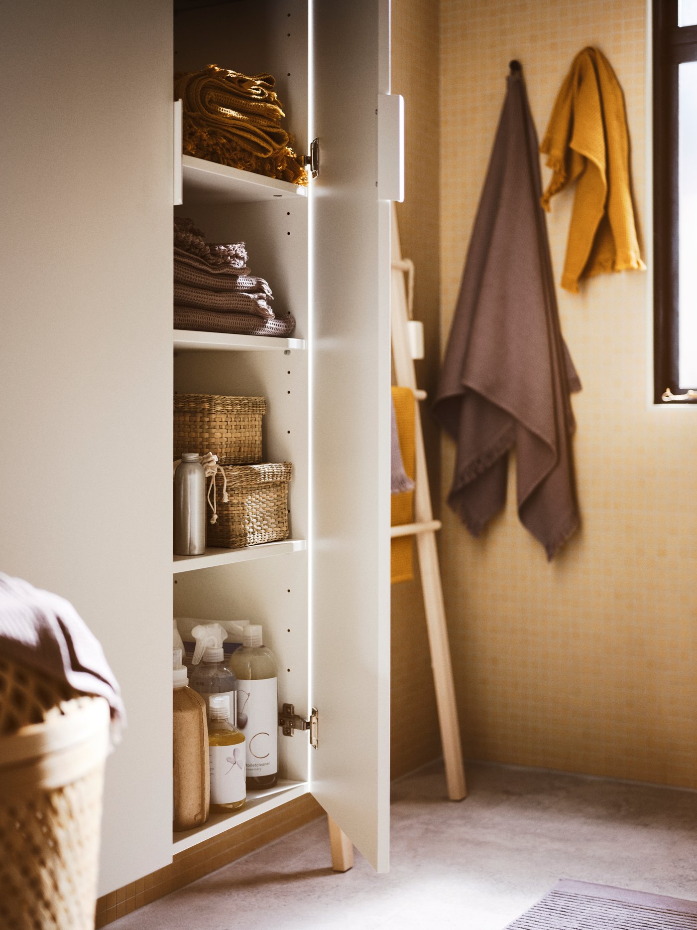 A bathroom with two white GODMORGON high cabinets with a door open with towels, boxes and cleaning products inside.