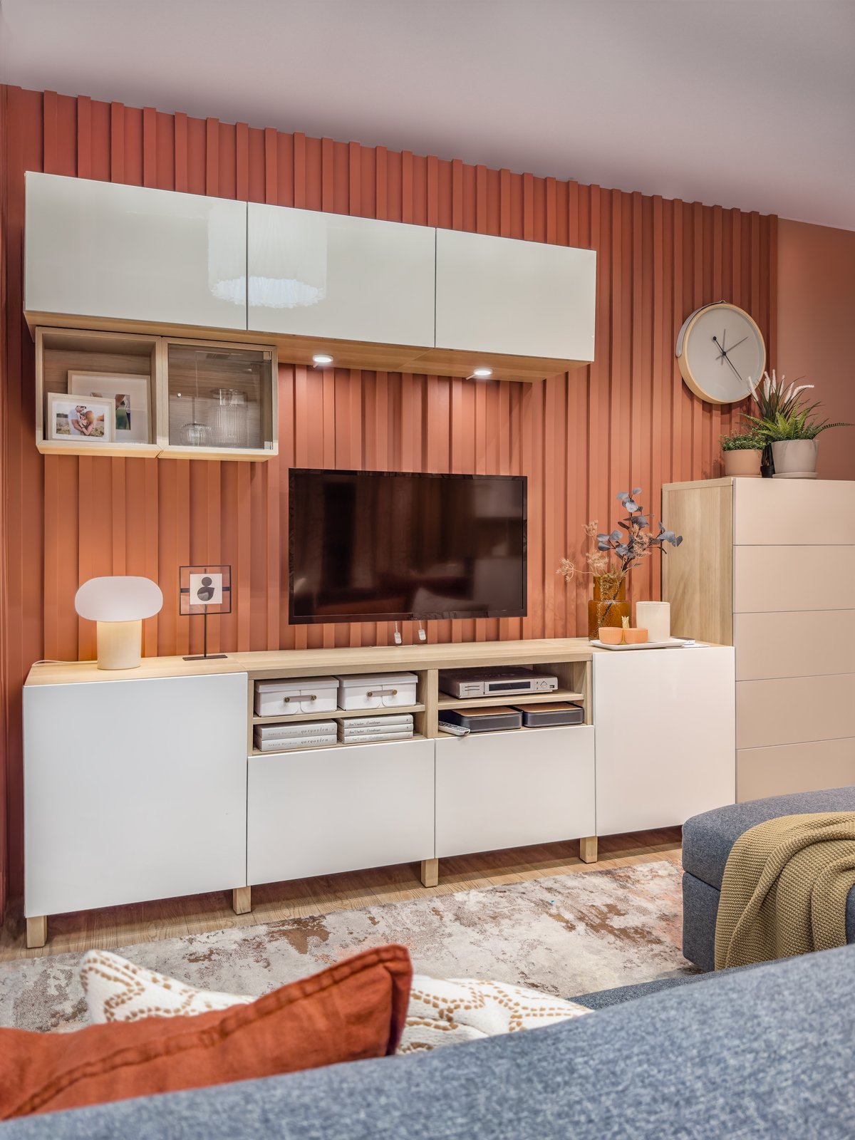 Kombinacja RTV z szafek modułowch BESTÅ na tle ściany z lamelami w kolrze terrakoty.