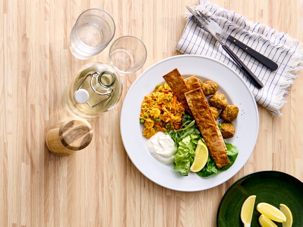 Falafel med ris og grønnsaker på en hvit tallerken på et spisebord av bjørk.