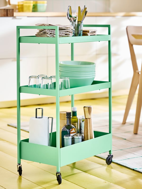 Light green NISSAFORS drinks trolley on wheels loaded with bowls, plates and other dinnerware in a modern kitchen setting.