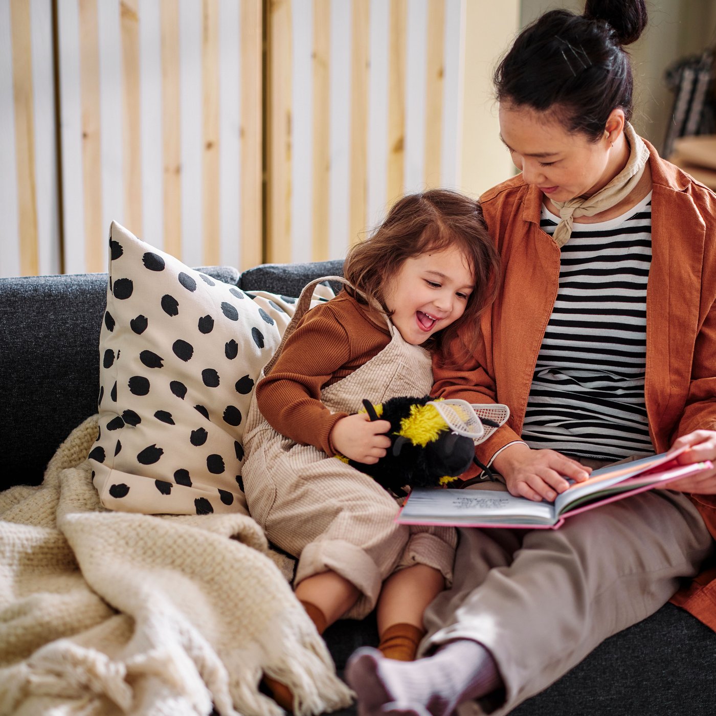 A person reads a story to a small child who is leaning against a cushion with an ODDNY cushion cover on a sofa.