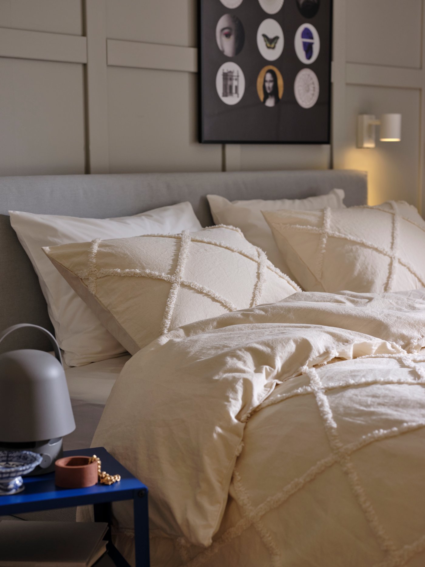 A light grey GLADSTAD upholstered bed covered with NYPONLUGGMAL bed linen with a bright blue KNARREVIK bedside table by it.