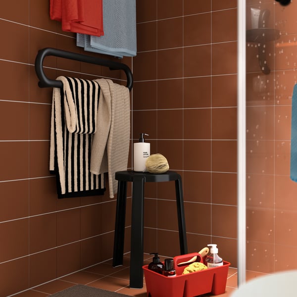 A black and beige striped SLÅNHÖSTMAL bath towel, draped on a black towel rail in a terracotta-tiled bathroom.