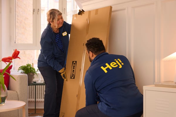 Zwei IKEA Mitarbeiter:innen liefern ein Paket in eine Wohnung