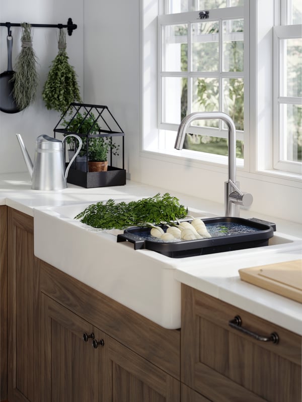 A white HAVSEN sink in a traditional style kitchen with an ÄLMAREN mixer tap and wash-up bowl in anthracite with vegetables.