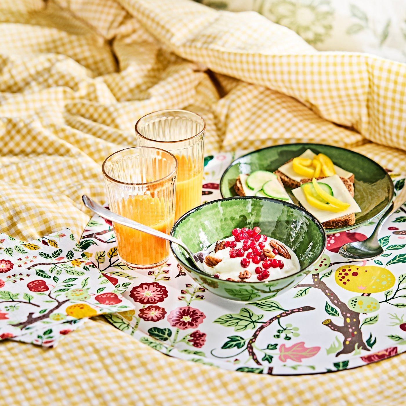 A HAVSBRAXEN tray with glasses and bowls containing breakfast foods, placed on a duvet cover with yellow and white pattern.