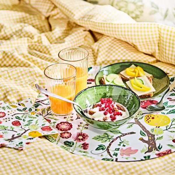 Plateau HAVSBRAXEN avec des verres et des bols contenant des aliments pour le déjeuner, sur une housse de couette au motif jaune et blanc.
