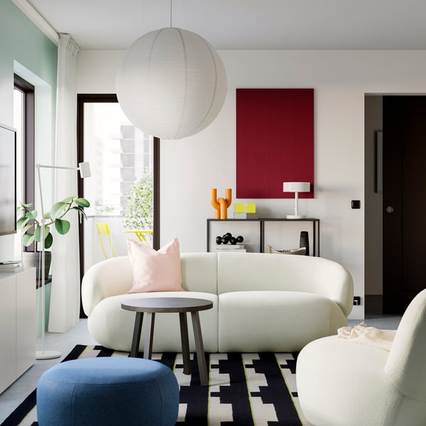 A LILLESÄTER pouffe and a coffee table stand in front of an off-white LILLESÄTER 3-seat sofa with an extra cushion on it.