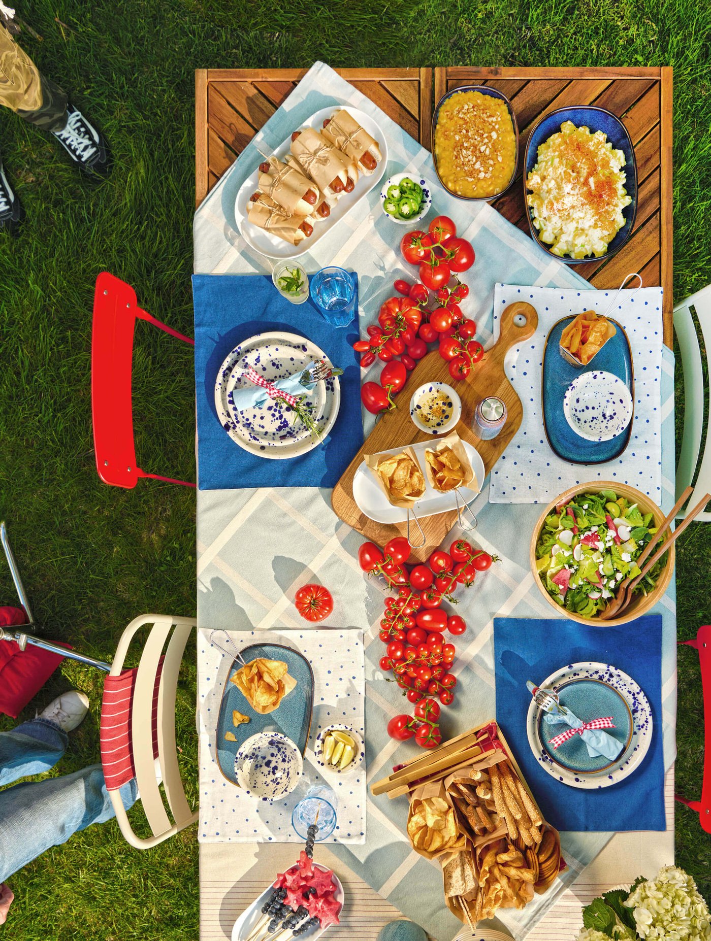 Overhead view of an outdoor picnic table with pastries, salads and fresh tomatoes on grass.