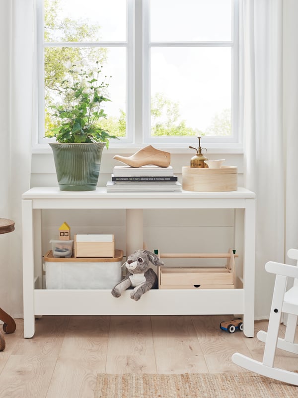 A HAVSTA console table with decorative objects on the top and children’s toys on the high-edged storage shelf beneath.