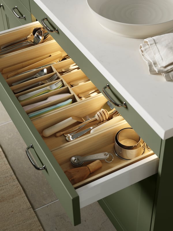 Un tiroir d’un meuble de cuisine est ouvert et les ustensiles de cuisine sont rangés dans un range-couverts UPPDATERA et deux range-ustensiles.