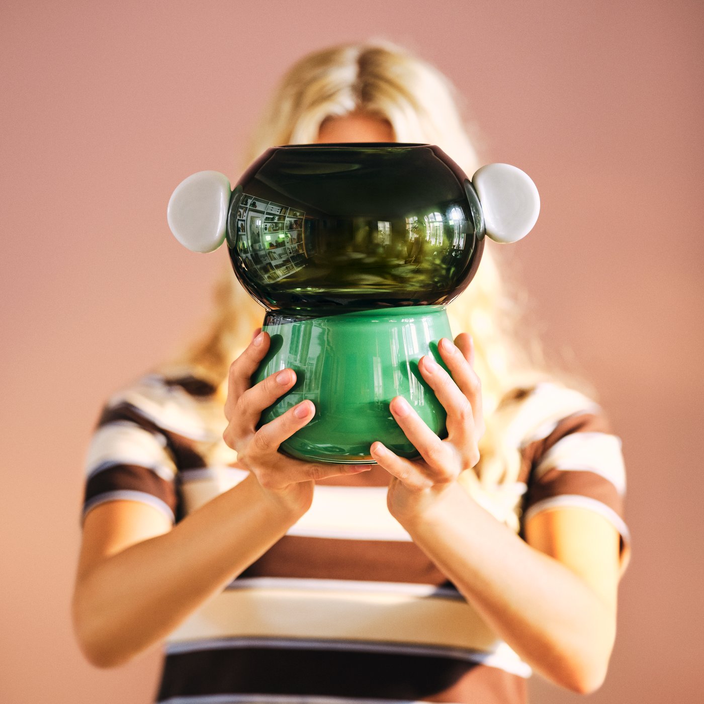 A person holds up a green, handblown IKEA PS 2026 vase in front of their face.