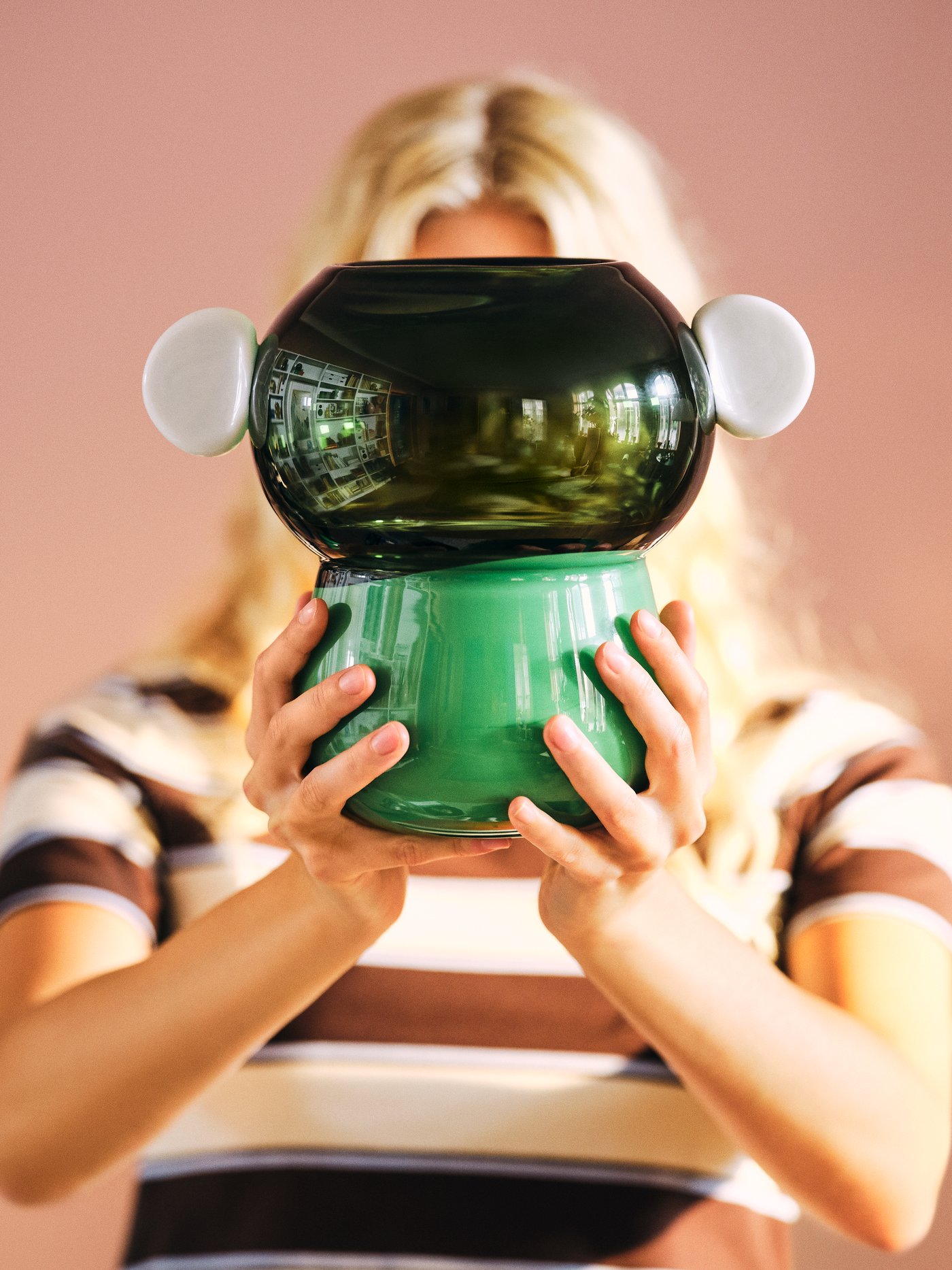 A person holds up a green, handblown IKEA PS 2026 vase in front of their face.
