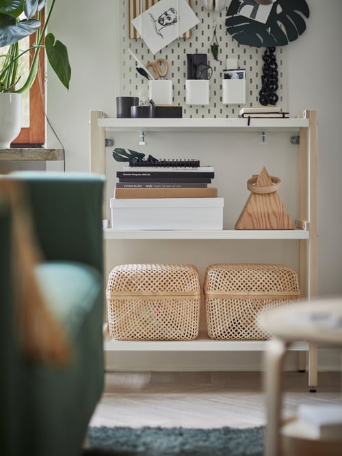 Das weiße EKENABBEN Regal ist hier in einem Wohnzimmer mit Körben, Büchern und Schreibutensilien zu sehen.