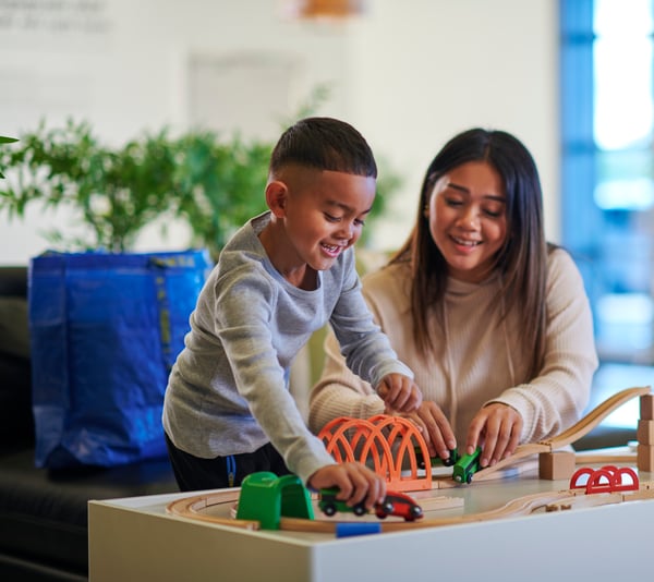 A mother and her son are playing with a wooden train set at an IKEA store.