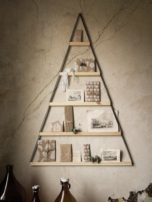 Decorazione triangolare in legno VINTER 2020 appesa a una parete, con piccoli pacchetti regalo e biglietti appoggiati sui pioli.