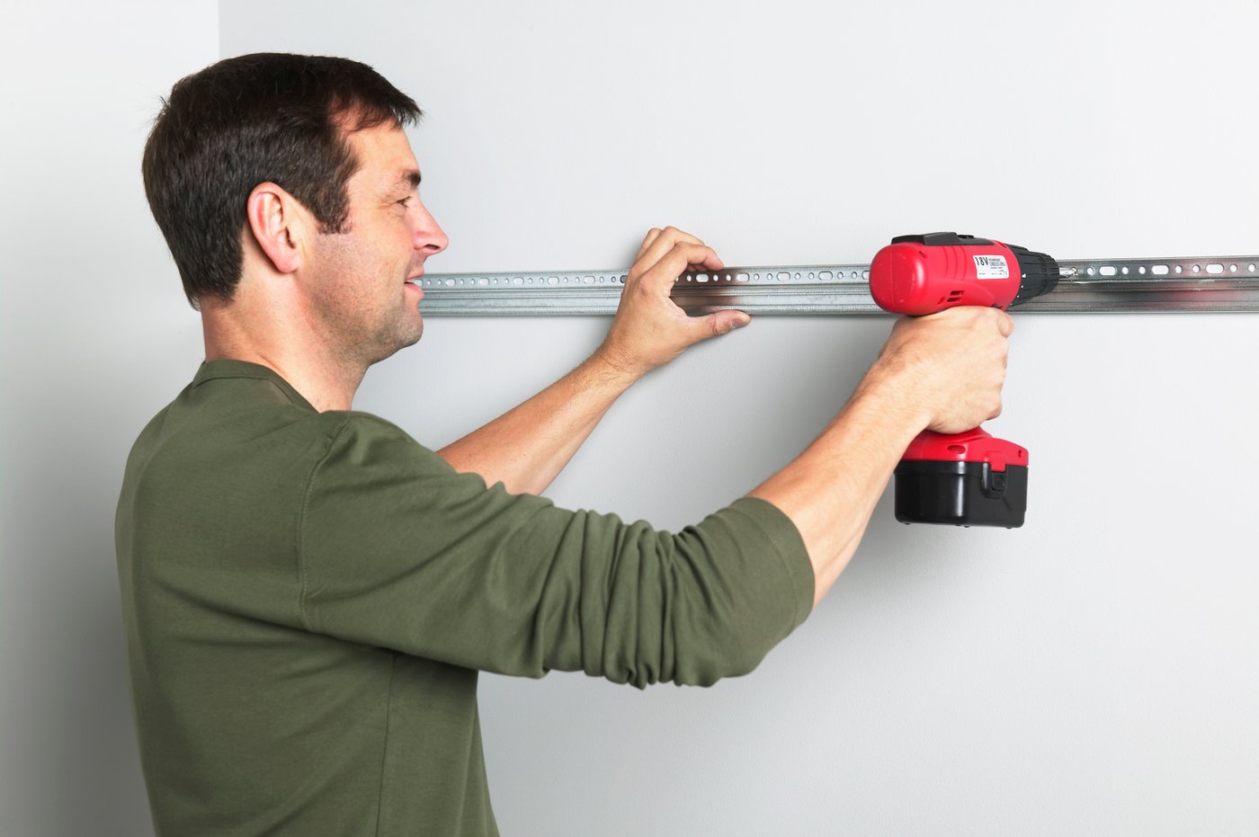 A man drilling a kitchen cabinet support rail to a wall.