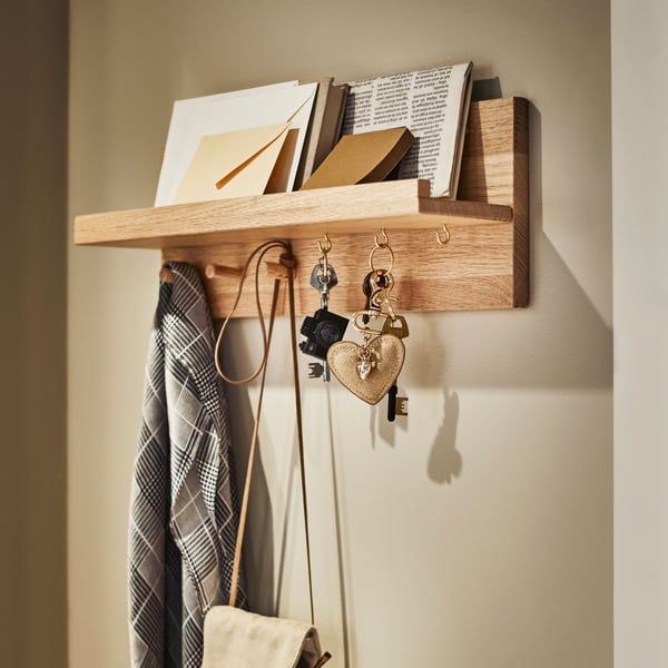 An oak HÄSTVISKARE wall organiser with hooks on a wall, with letters on its shelf and keys, a bag and a scarf on its hooks.
