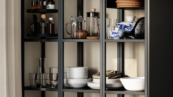 ENHET high frame wall shelves filled with glasses, plates, bowls, and bottles. Open shelving showcases a mix of kitchenware. 