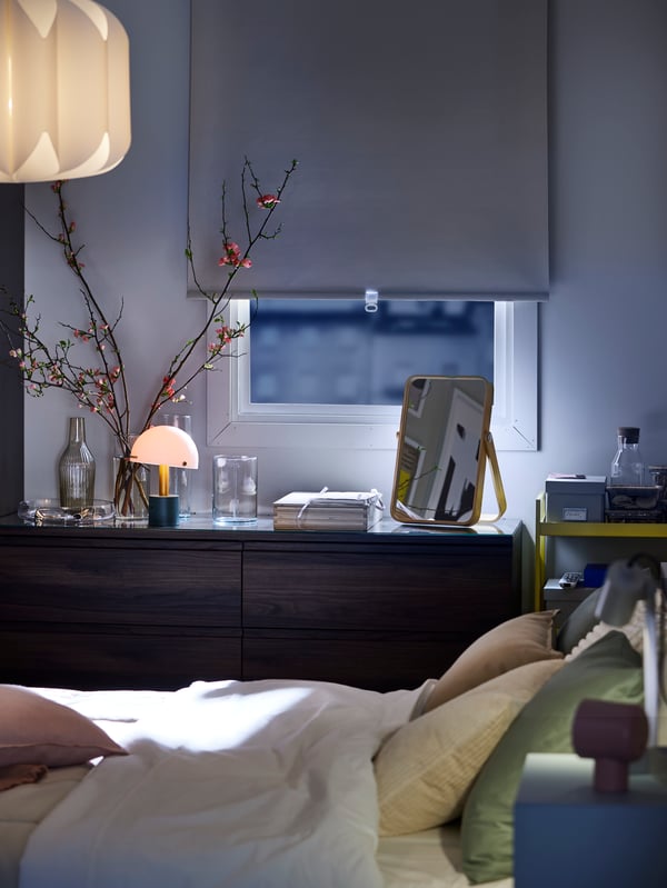 A beige FÖNSTERBLAD block-out roller blind halfway down on a window which has two STORKLINTA chests with 3 drawers in front.