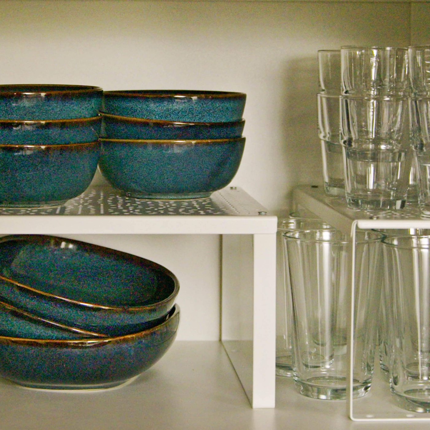 Stacked blue ceramic bowls and clear glasses organized on white cabinet shelves.