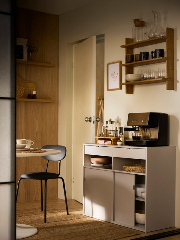 Part of a softly sun-dappled dining area with dining accessories in, on and around a light-grey SPIKSMED sideboard.