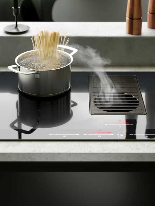 Ein HEMKOMST Topf mit Spaghetti ist hier auf einem FÖRNEBO Induktionskochfeld mit integriertem Dunstabzug zu sehen. Dahinter steht ein FULLTALIG Kerzenständer.