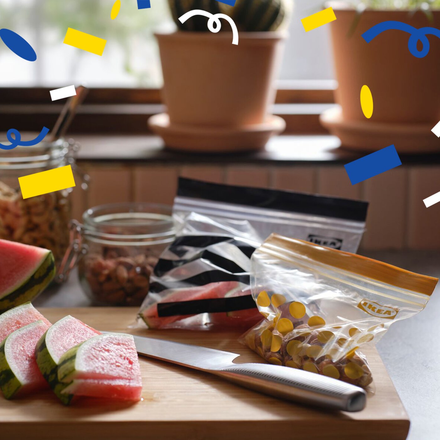 Wassermelonenscheiben, ein Messer und zwei unterschiedlich große, wiederverschließbare ISTAD Kunststoffbeutel liegen auf einem Schneidebrett in einer Küche. Von oben flieben blauen, weiße und gelbe Konfetti herunter.