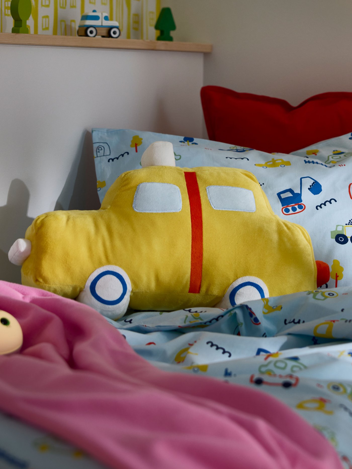En barnsäng med färgglada textilier och en kudde formad som en gul bil.