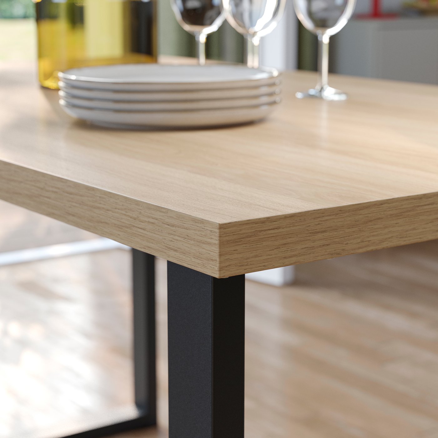 The edge of a SKÅLSTA table highlighting the paper foil material of the table top, with stacked plates and wine glasses on it.