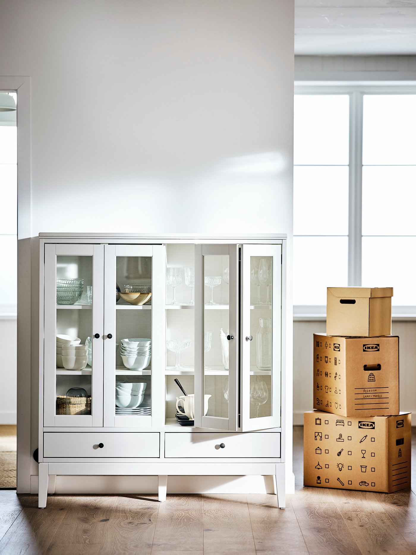 Living con un armario blanco con dos puertas de vidrio plegadas de madera maciza y vidrio templado con cuencos y vasos en su interior.