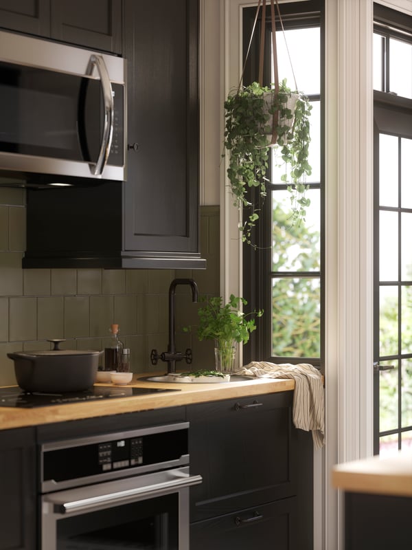 Des électroménagers et un évier avec un mitigeur noir se trouvent dans une cuisine avec des façades LERHYTTAN teintées noires.