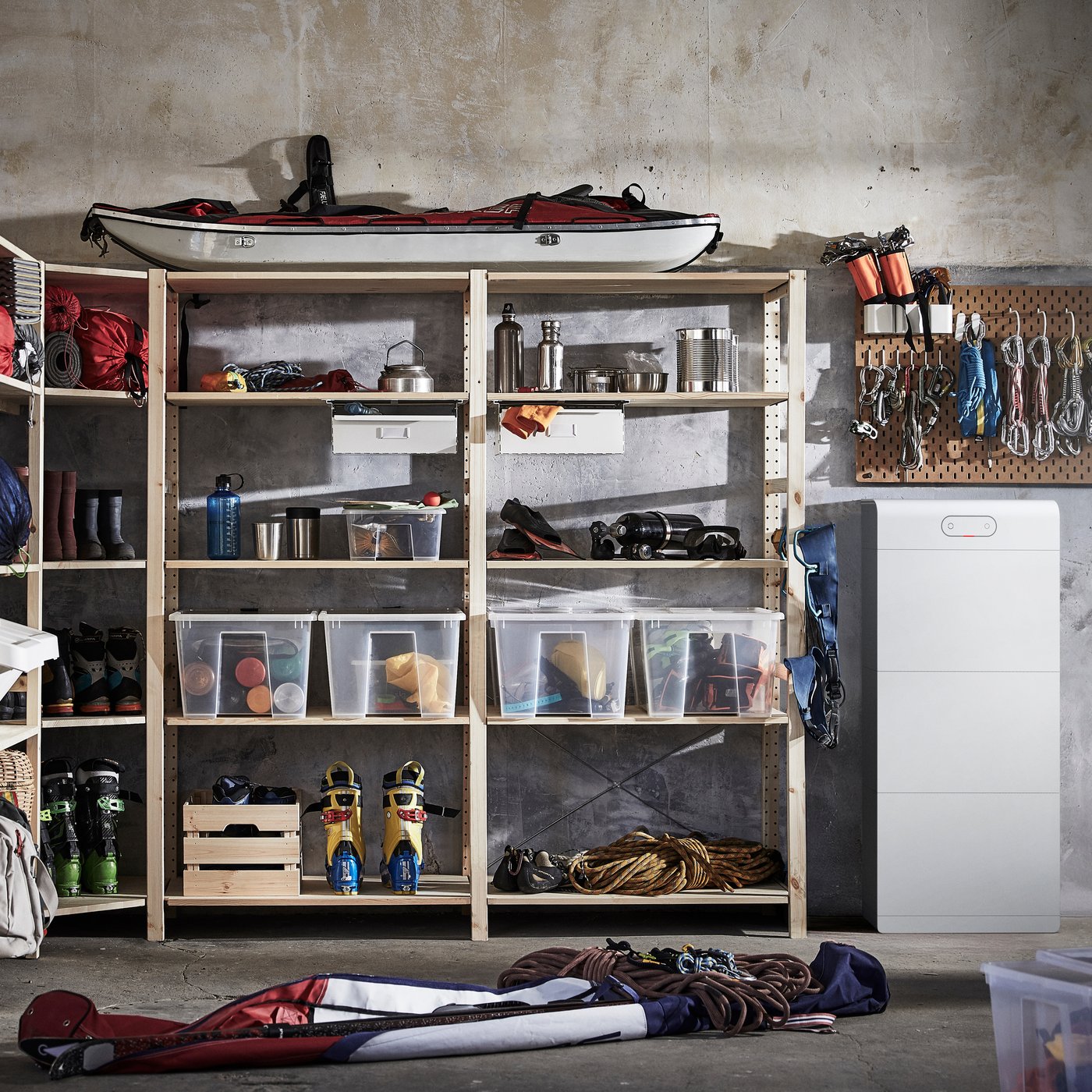 Een overzichtelijke opslag in de garage met rekken, sport- en outdooruitrusting, doorzichtige opbergdozen en een witte kast tegen een betonnen muur.