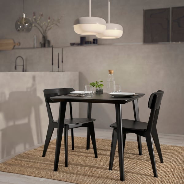 A square black/ash veneer LISABO dining table with two matching chairs in a room with concrete grey walls and a jute rug.